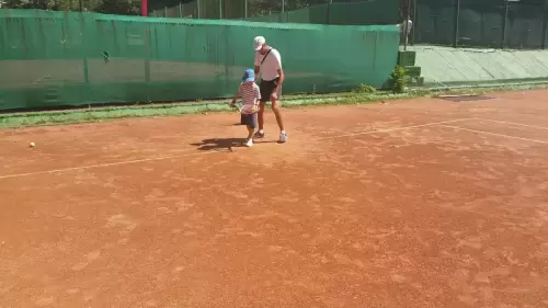 Antrenor de tenis oferind instrucțiuni unui copil pe teren, explicând tehnica corectă de lovitură