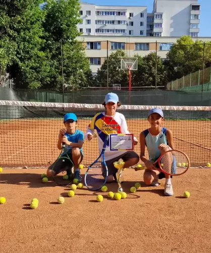 Trei copii pe terenul de tenis, ținând cupe și medalii câștigate la Campionatul Național de Juniori