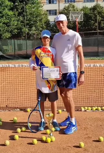 Antrenor de tenis și un copil pe teren, purtând un tricou cu inscripția „Campion Național” la Campionatele Naționale de Juniori