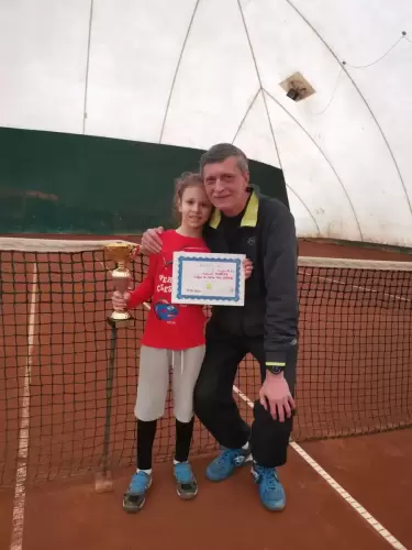 Antrenor de tenis și un copil sportiv pe teren, cu o cupă și o diplomă, după terminarea competiției
