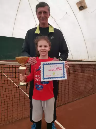 Antrenor de tenis și un copil sportiv pe teren, cu o cupă și o diplomă, după terminarea competiției