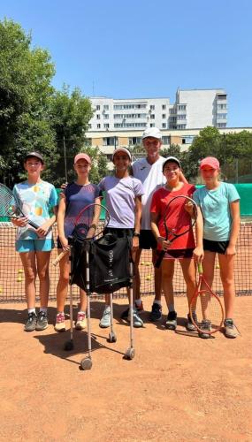 Antrenor de tenis și cinci copii fericiți lângă fileu, în timpul unei pauze la antrenament